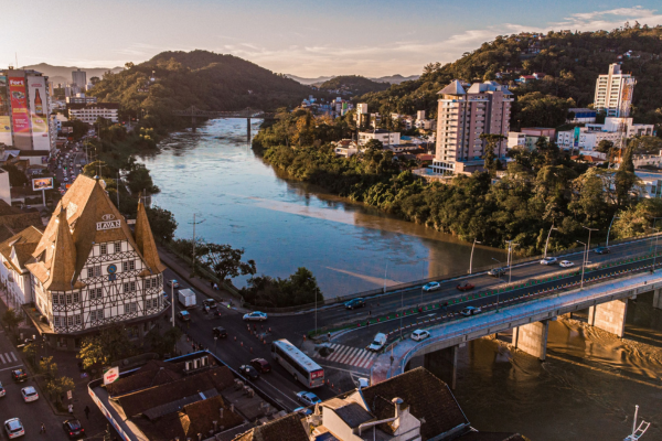 Aerial view of downtown Blumenau featuring traditional German half-timbered architecture, the Itajaí-Açu River, and surrounding green hills at golden hour in Santa Catarina, Brazil.